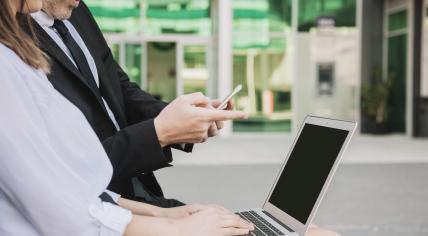 A woman and man working together on a project using an iPhone and a Macbook Air