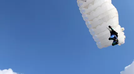 Parachutist with white parachute on blue sky