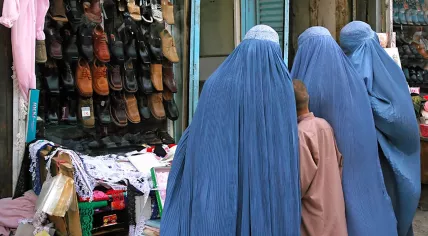 Three Afghan women and a young boy standing outside a shoe store in Kabul, Afghanistan. The women are wearing blue burqas (burkas).