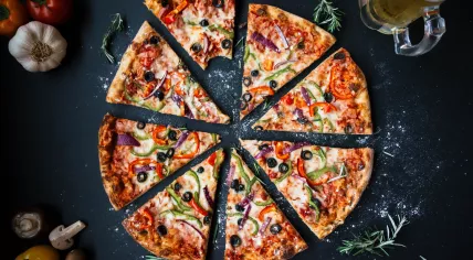 A beer and a vegetable pizza loaded with red pepper, green pepper, red onion and black olives