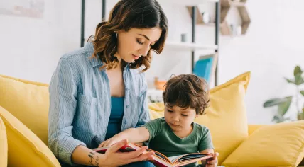 Mother reading to a young child while sitting on a yellow couch