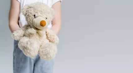 Partial view of child holding teddy bear isolated on grey