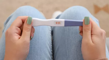 Selective view of a young woman's hands holding a positive pregnancy test on her lap