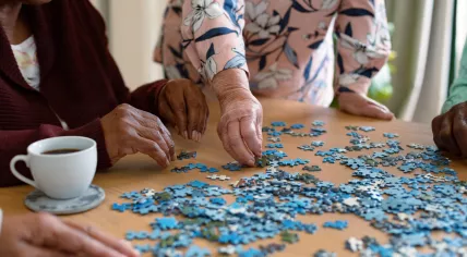 Selective view of four elderly people sitting at a table and building a puzzle