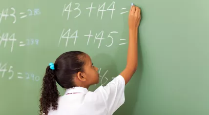 Primary school girl writing maths answer on chalkboard