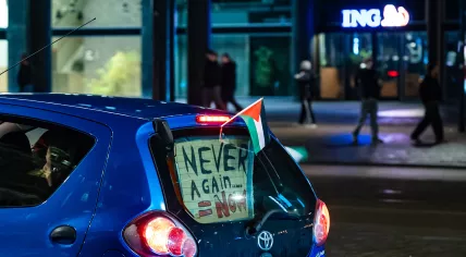 A blue car with Palestinian flags and a sign reading "never again" driving over the Coolsingel in Rotterdam as local Palestinians celebrate a ceasefire agreement between Israel and Hamas, 15 January 2025