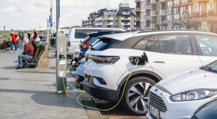 Parking: A Volkswagen VW ID electric car charging in a large parking lot near the sea in Egmond aan Zee, with people in the background. 25 August 2024