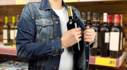 A man is stealing an alcohol bottle from a store.