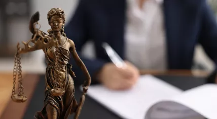 Cropped shot of a lawyer writing and Lady Justice statue on a table.
