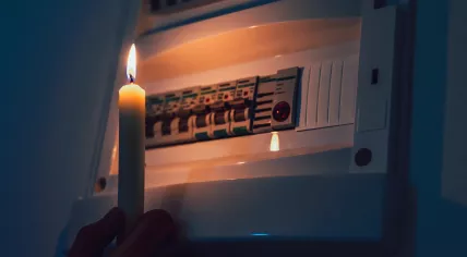 A candle is used to inspect a fuse box during a power outage.