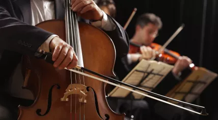 A cellist performs in the foreground, with two violinists partially visible behind