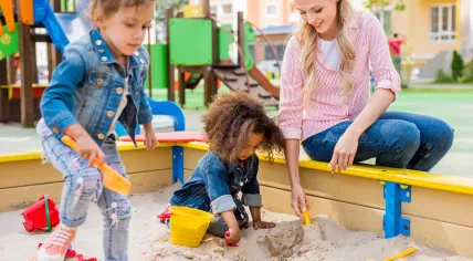 Woman playing with two young children at a playground