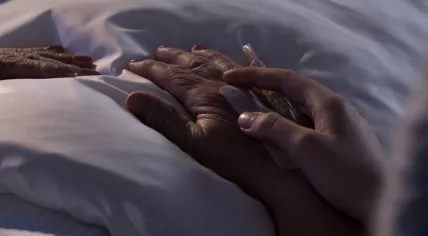 Hospice concept: Someone holding the hand of an elderly person in a bed