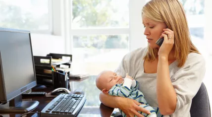 A woman works from home while looking after her baby.