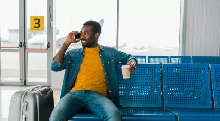 A traveler talks on the phone and drinks coffee while waiting for his flight.