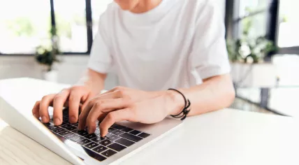 Partial view of teen boy in white t-shirt using laptop