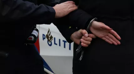 Arrest: Police officer handcuffing a suspect with a police car in the background