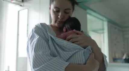 A mother and newborn baby, wrapped in a striped hospital gown