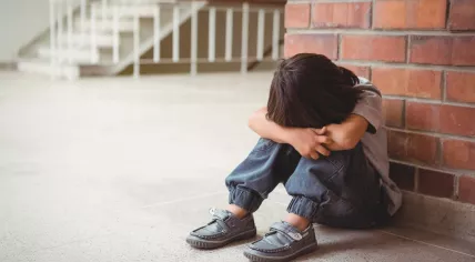 A sad child sits alone in a school corridor.