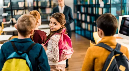 Boys and girls enter a classroom and are greeted by their teacher.