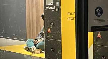 A person takes shelter from the cold wind on Christmas Eve inside a Geldmaat ATM storefront location in Amsterdam. 24 Dec. 2025
