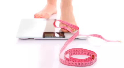 Female feet stepping onto a bathroom scale with measuring tape nearby
