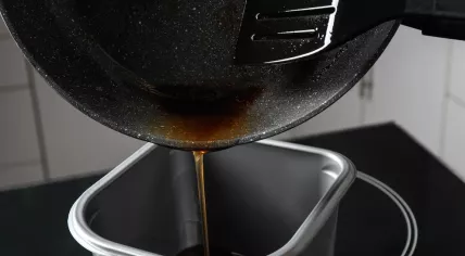 Pouring used cooking oil from frying pan into container