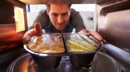 A man is taking a plastic container out of the microwave