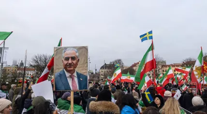 A woman holds a placard showing Reza Pahlavi during an anti-Iranian regime protest in Gothenburg, Sweden at Bältespännarparken in Gothenburg, Sweden on January 17, 2026, while others wave the Lion and Sun flag.