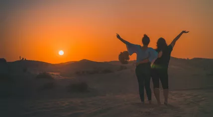 Two women standing in the desert at sunset in Dubai, United Arab Emirates. 2022