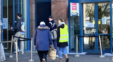 An election monitor escorts a handful of voters into the polling place at the Muiderkerk in Amsterdam-Oost. 18 March 2026