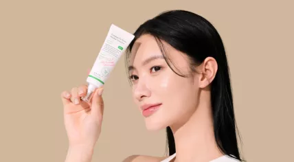 A promotional photo of a woman holding a bottle of AXIS-Y Complete No-Stress Physical Sunscreen