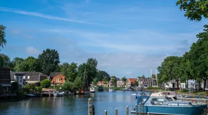Canal in the village of Blokzijl, Overijssel, lined with moored boats, traditional houses, and a white drawbridge under a clear summer sky
