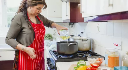 Woman cooking in the kitchen, adding oil to the pot with sliced up bell peppers on the counter
