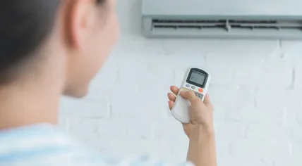 An image showcasing a woman using a remote control to adjust a wall-mounted air conditioner.