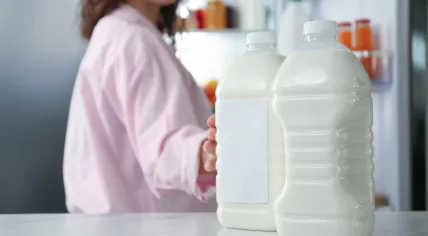 A woman reaches out for a plastic milk bottle in the fridge.