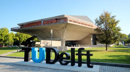 A TU/Delft sign on the university's campus in front of the auditorium.