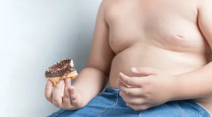 Childhood obesity: Partial view of an overweight boy holding a donut