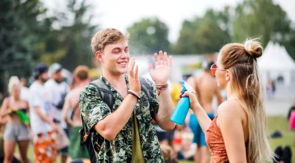 A girl sprays a guy with water at a festival.