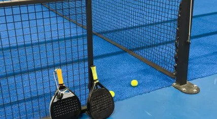 Two padel rackets on a padel blue court with several yellow balls.