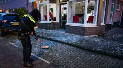 A police officer sweeping up glass from a window shattered in an explosive attack