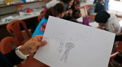 A_girl_holds_up_a_drawing_of_a_bride_and_groom_during_a_discussion_about_child_marriage_with_teenage_Syrian_refugee_girls_in_a_community_centre_in_southern_Lebanon_(14680478784)