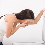 Woman vomiting over toilet.