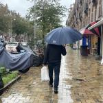 A man with an umbrella walks past covered scooters on a cloudy, rainy day in Amsterdam Oost, 20 October 2023