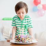A 4-year-old boy in a green shirt blowing out the candles on his birthday cake