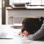 Young tired woman resting her head on her arms at her office desk