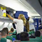 A flight attendant helps a passenger stow carry-on luggage in a plane's overhead compartment