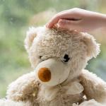 Cropped view of child touching teddy bear near blurred window with raindrops