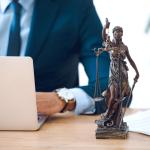 Cropped shot of lawyer using laptop and lady justice statue on table.