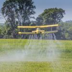 A yellow crop duster spraying pesticides on a field